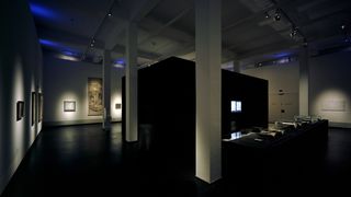 Ein dunkler Ausstellungsraum in dessen Mitte ein weiterer, schwarzer, quadratisch, abgetrennter Raum ist.