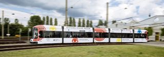 Eine Straßenbahn fährt durch das Bild, auf der Werbung des Hygiene-Museums steht.