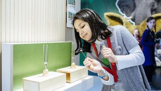 Ein Mädchen schlägt gegen zwei Stimmgabeln, die auf Holzblöcken aufgebaut sind.