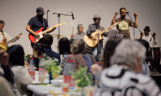 Mitglieder der Community Werkstatt klatschen, essen und hören einer Musikband zu
